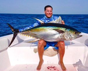 Angler kneeling with a large yellowfin tuna on a boat, caught on a Hamachi rod
