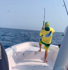 Angler fighting a tuna on a Hamachi rod from the bow of a boat, rod bent high overhead