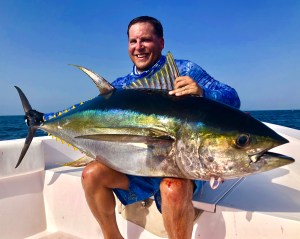 Smiling angler holding a yellowfin tuna on a boat, caught on a Hamachi rod